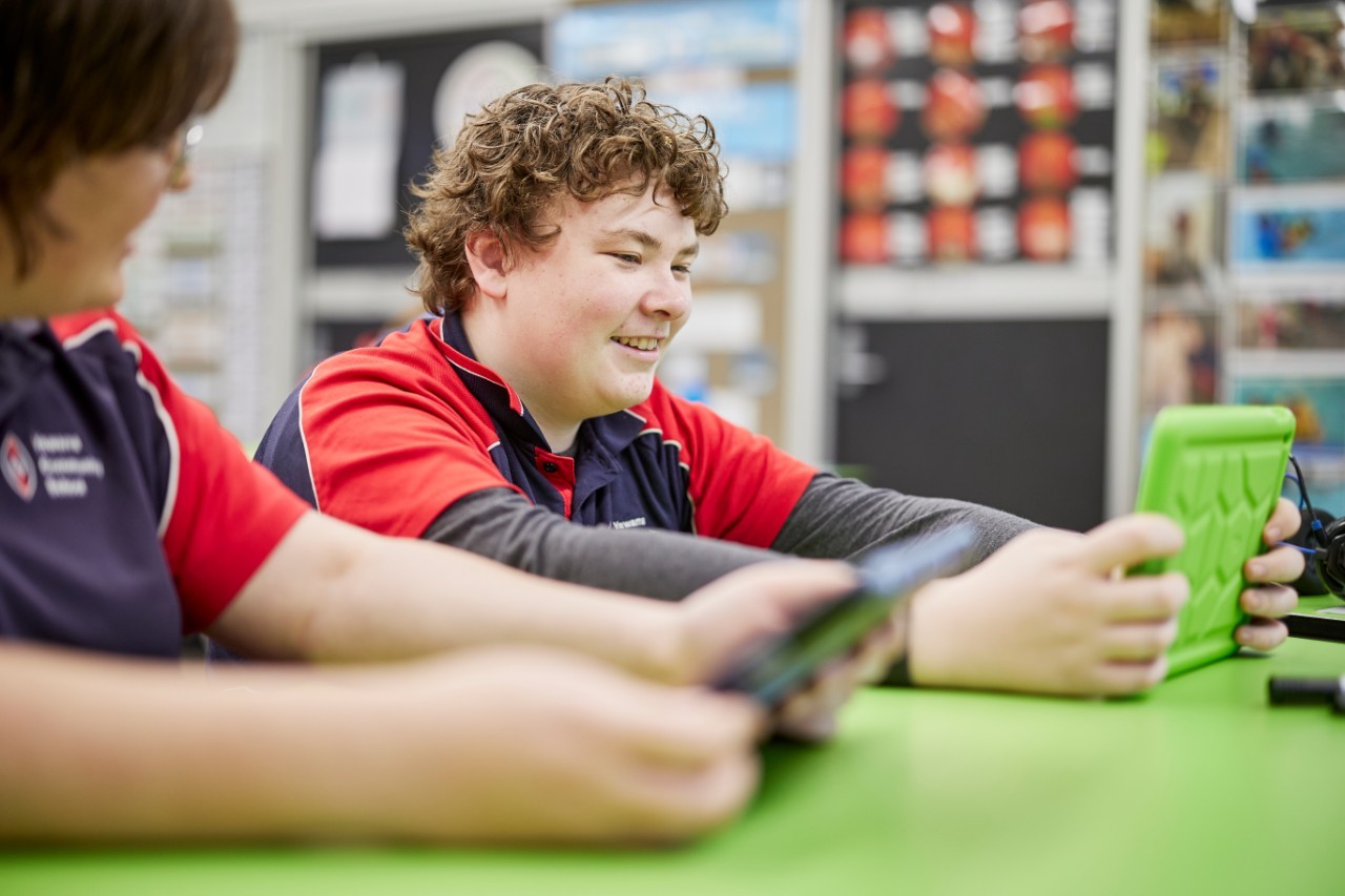 Two male students holding and looking at their tablets in a school classroom.